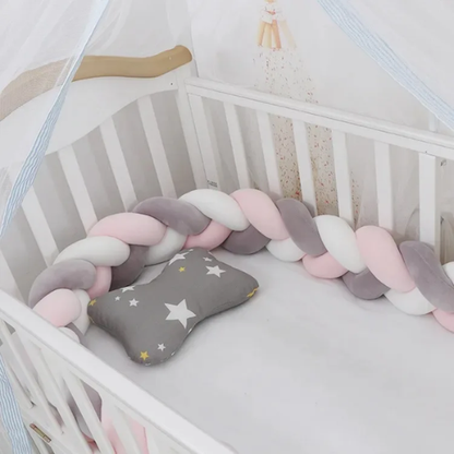 Tour de lit bébé tressé 3 brins aux couleurs rose poudré, gris et blanc, installé dans un berceau en bois avec un coussin à étoiles.